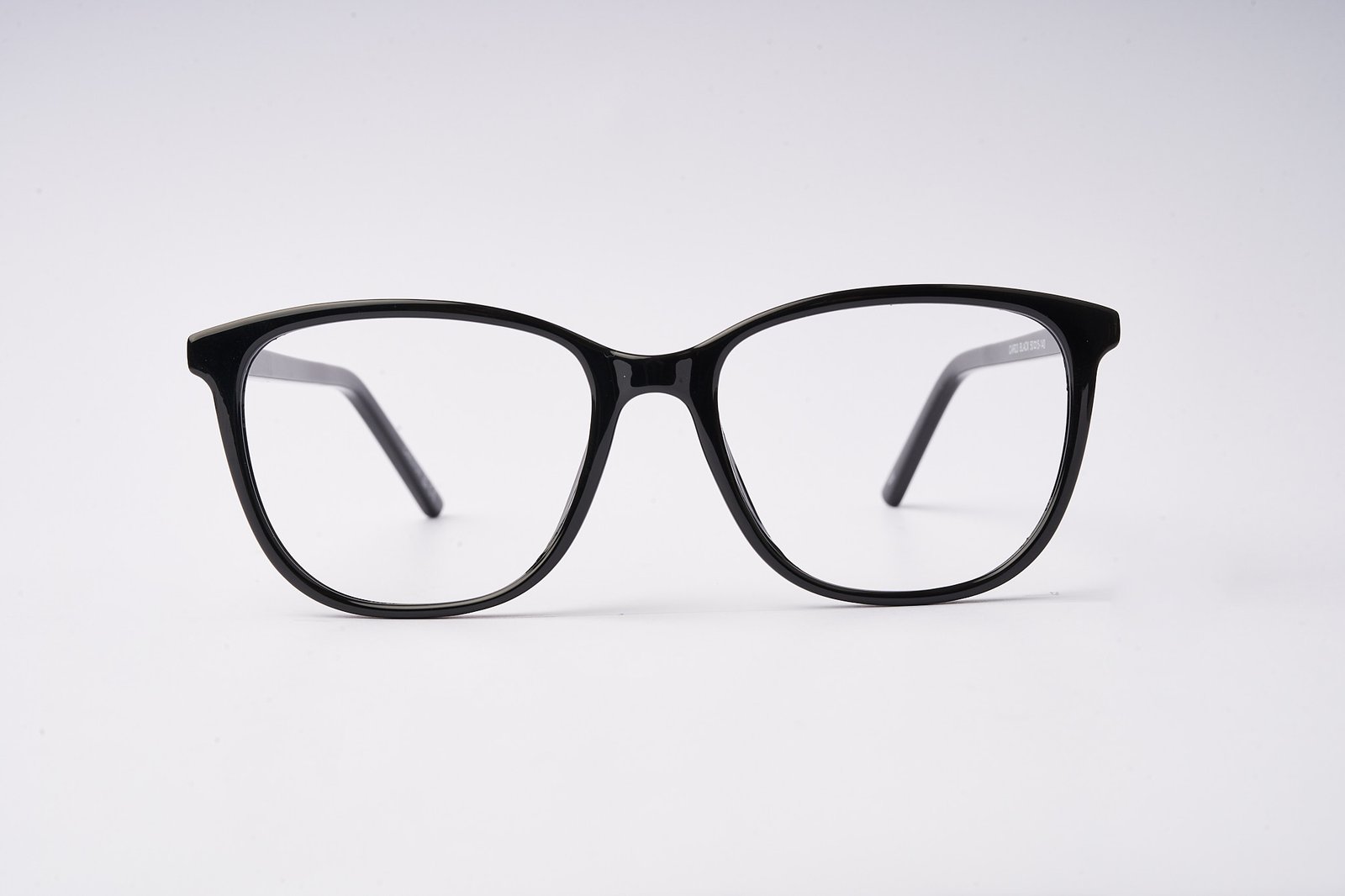 Close-up of black eyeglass frames with rounded lenses against a white background, showing the bridge and top rims.